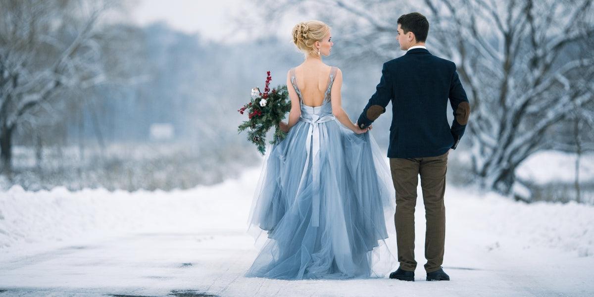 ride and groom are holding hands and walk the snowy road. View from back. Winter wedding outdoors.