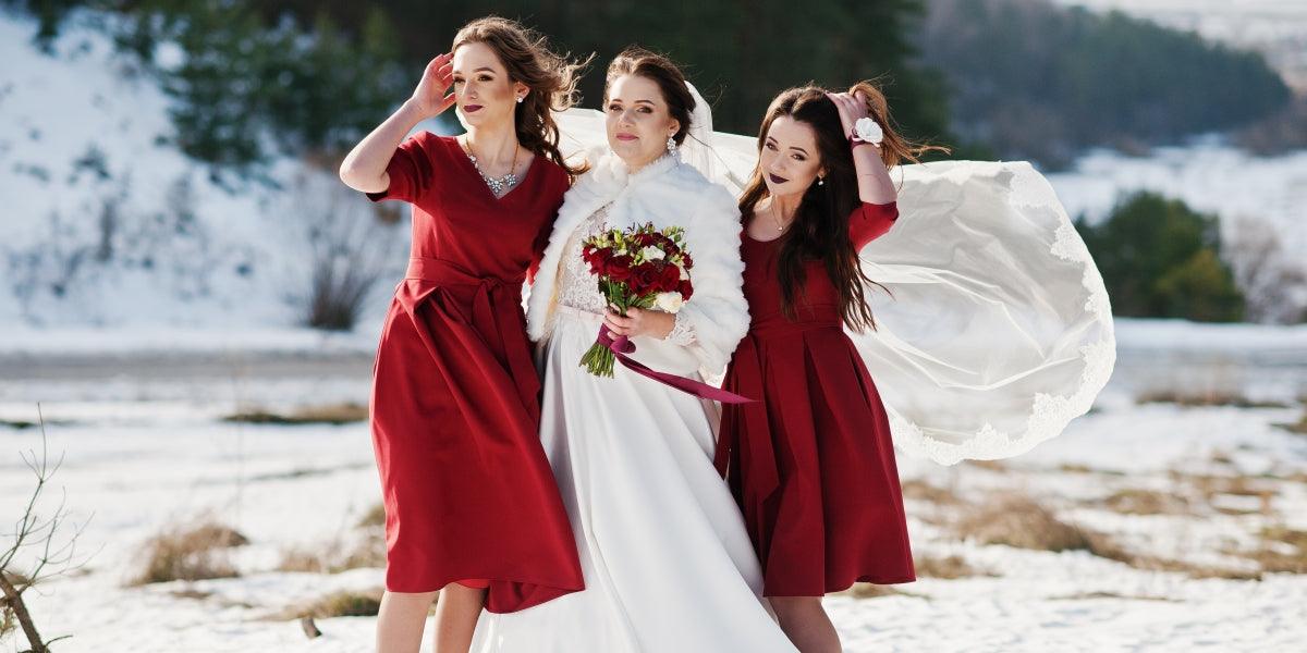 Pretty bridesmaids on red dresses with bride on sunny winter wedding day.